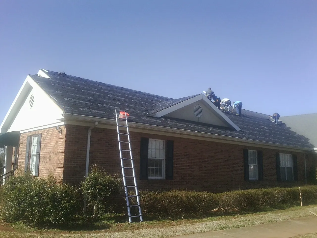 Crew tearing shingles off a brick ranch roof with a ladder set — Emergency Roof Repair work by our crew in Urbana